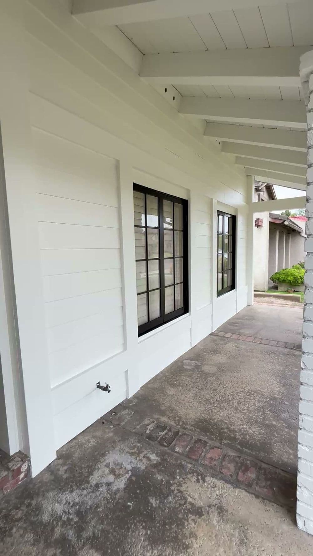 Modern white exterior with black windows and a covered porch, featuring brick accents.