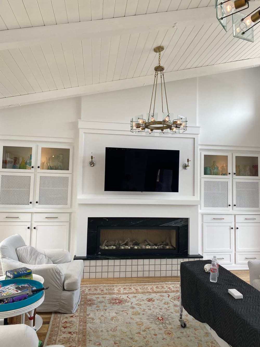 Bright modern living room with a fireplace, TV, white beams, and stylish decor elements.