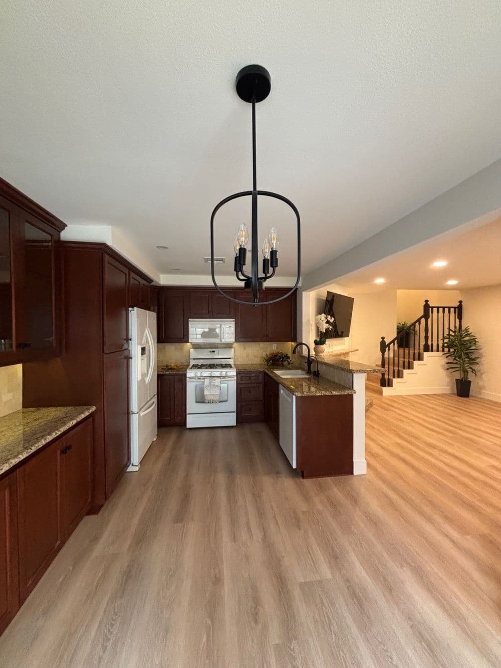 Modern kitchen with dark wood cabinetry, granite countertops, and stylish chandelier.